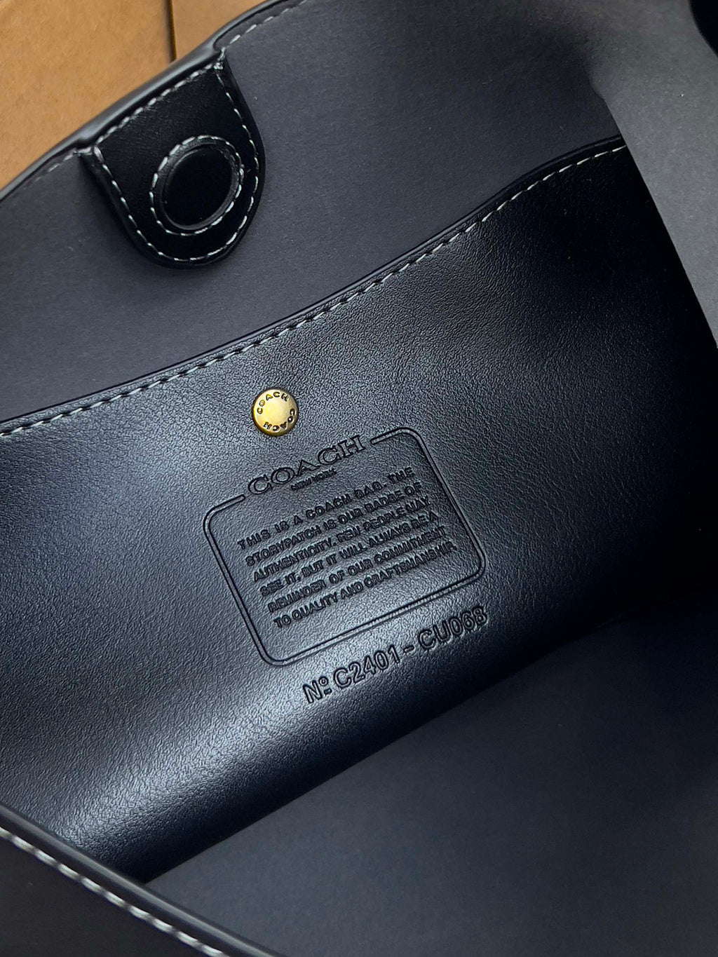 Dark leather handbag close-up with stitched label patch and metal rivet