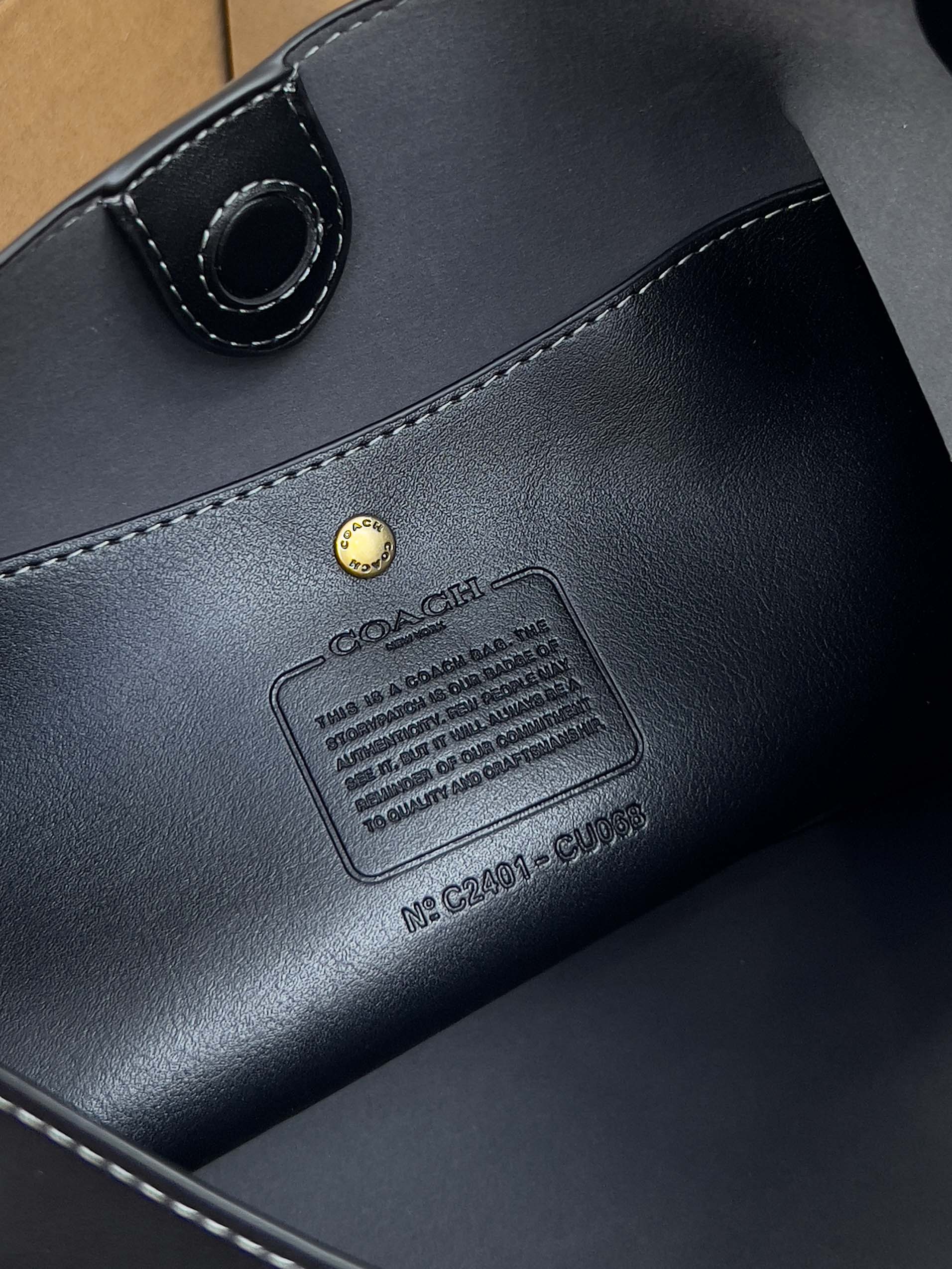Dark leather handbag close-up with stitched label patch and metal rivet