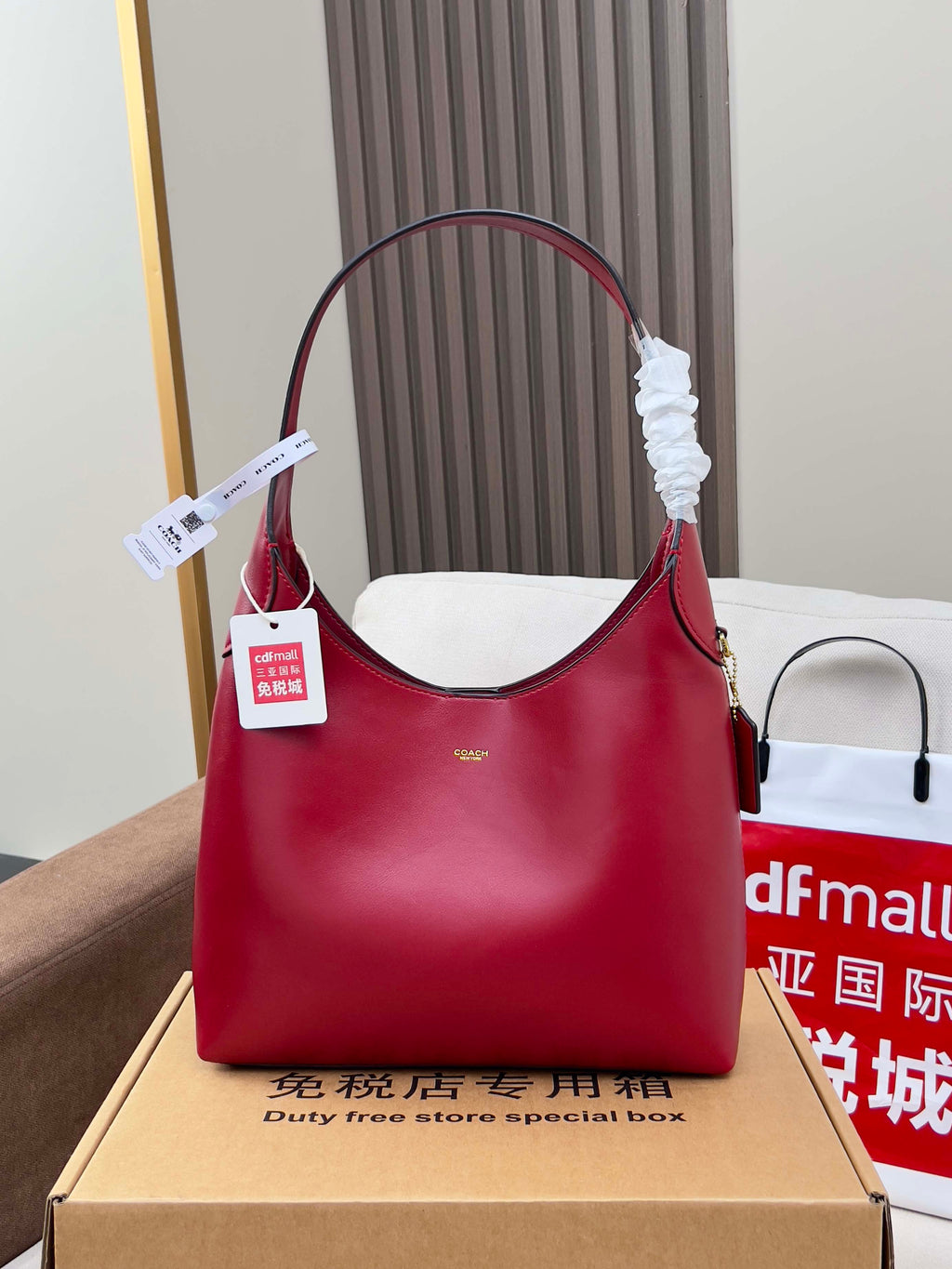 Red leather bucket-style bag with top handle, shown on gift box