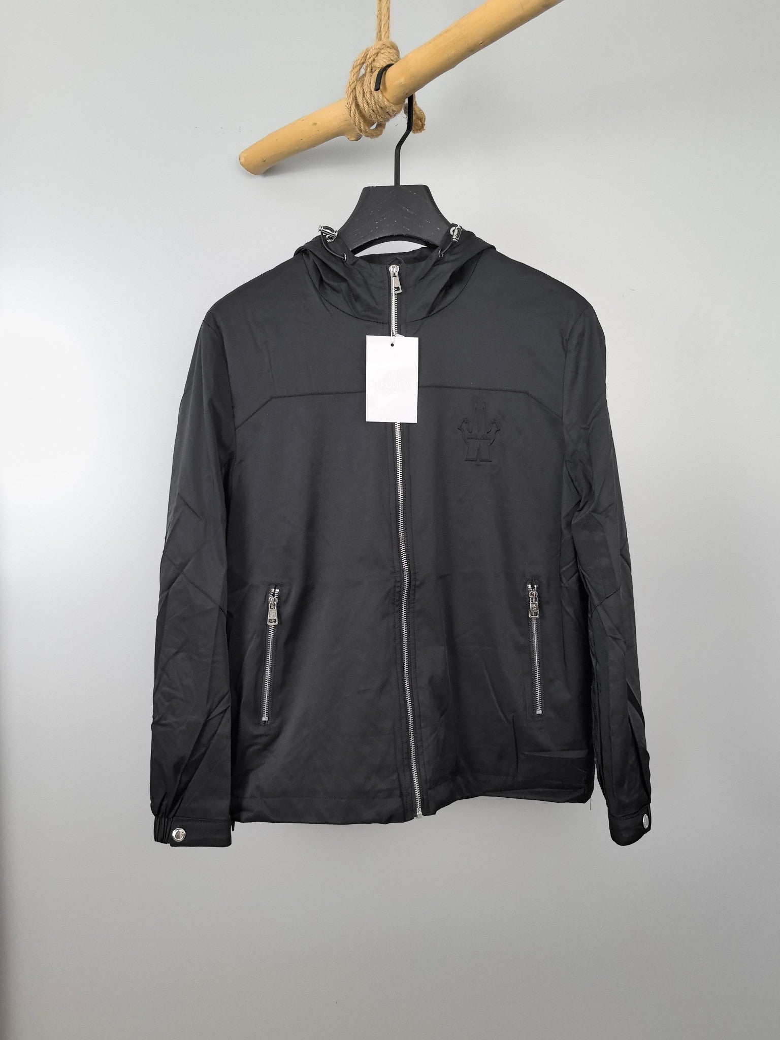 Black long hooded jacket with front zip and side pockets, hanging tag.