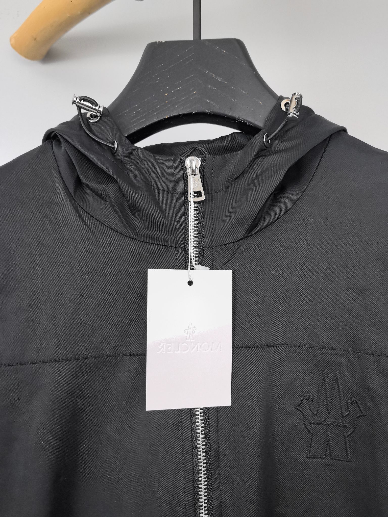Black hooded jacket close-up with front zipper and hanging white tag.