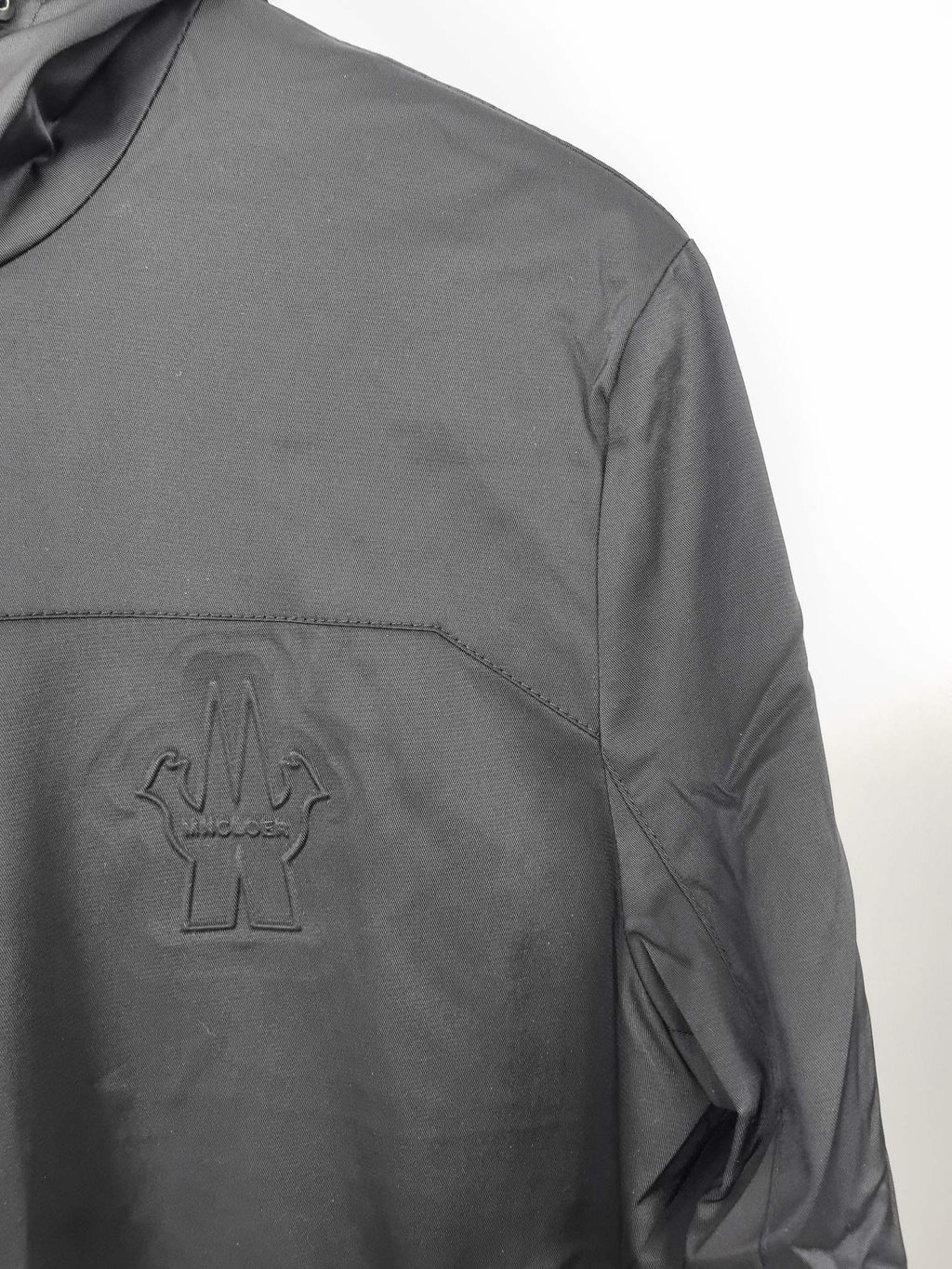 Black hooded jacket chest logo patch with curved seam detail.