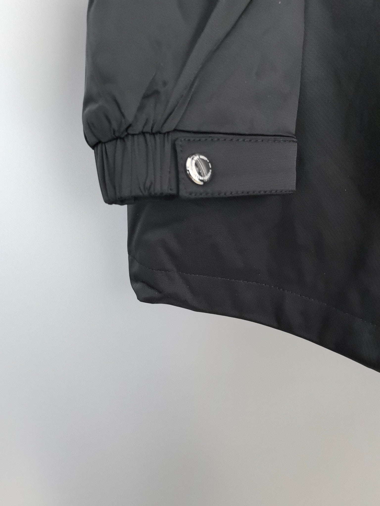 Black long jacket sleeve cuff with snap button and gathered hem.