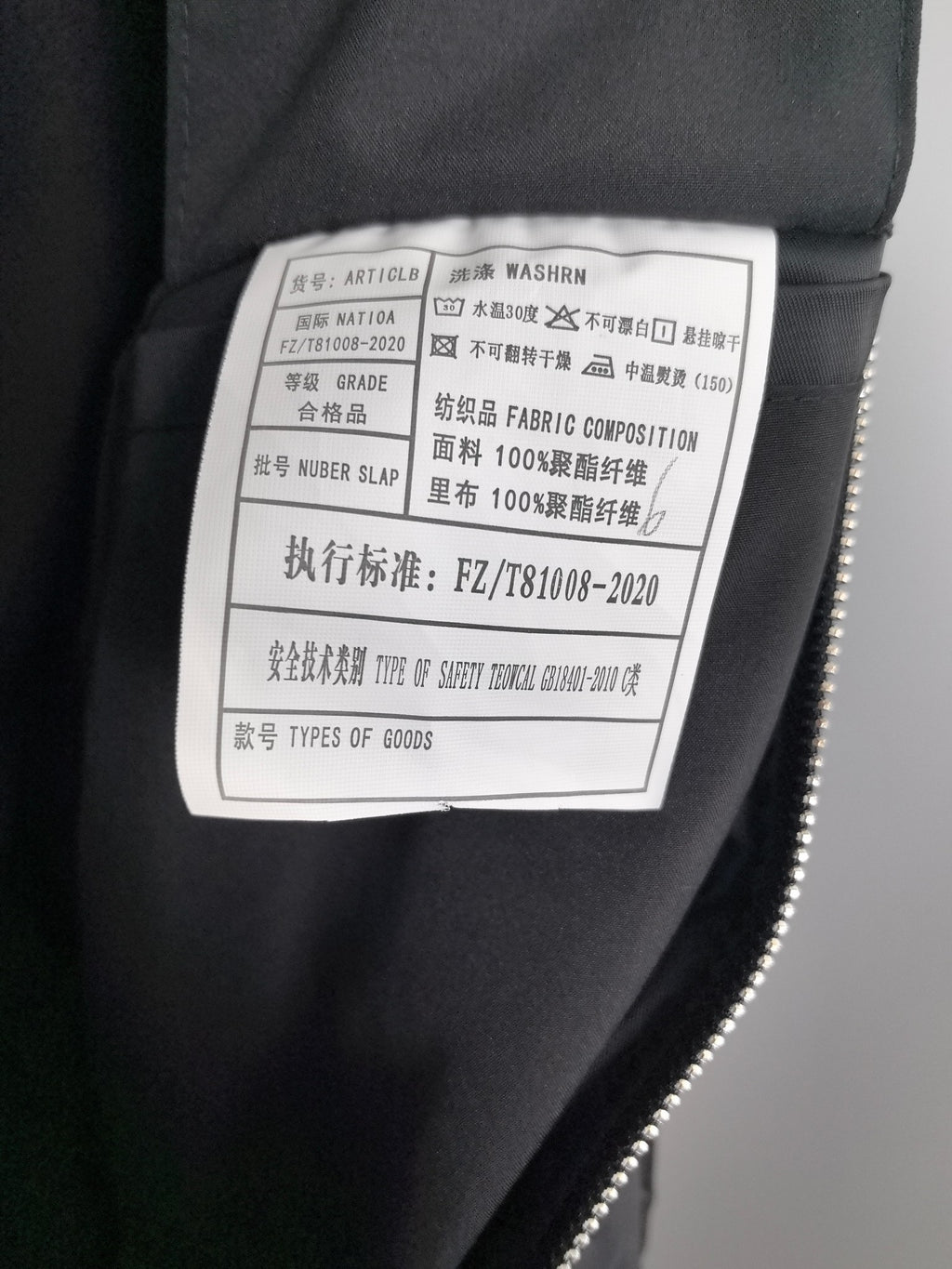 Black jacket care label with fabric composition and washing instructions.