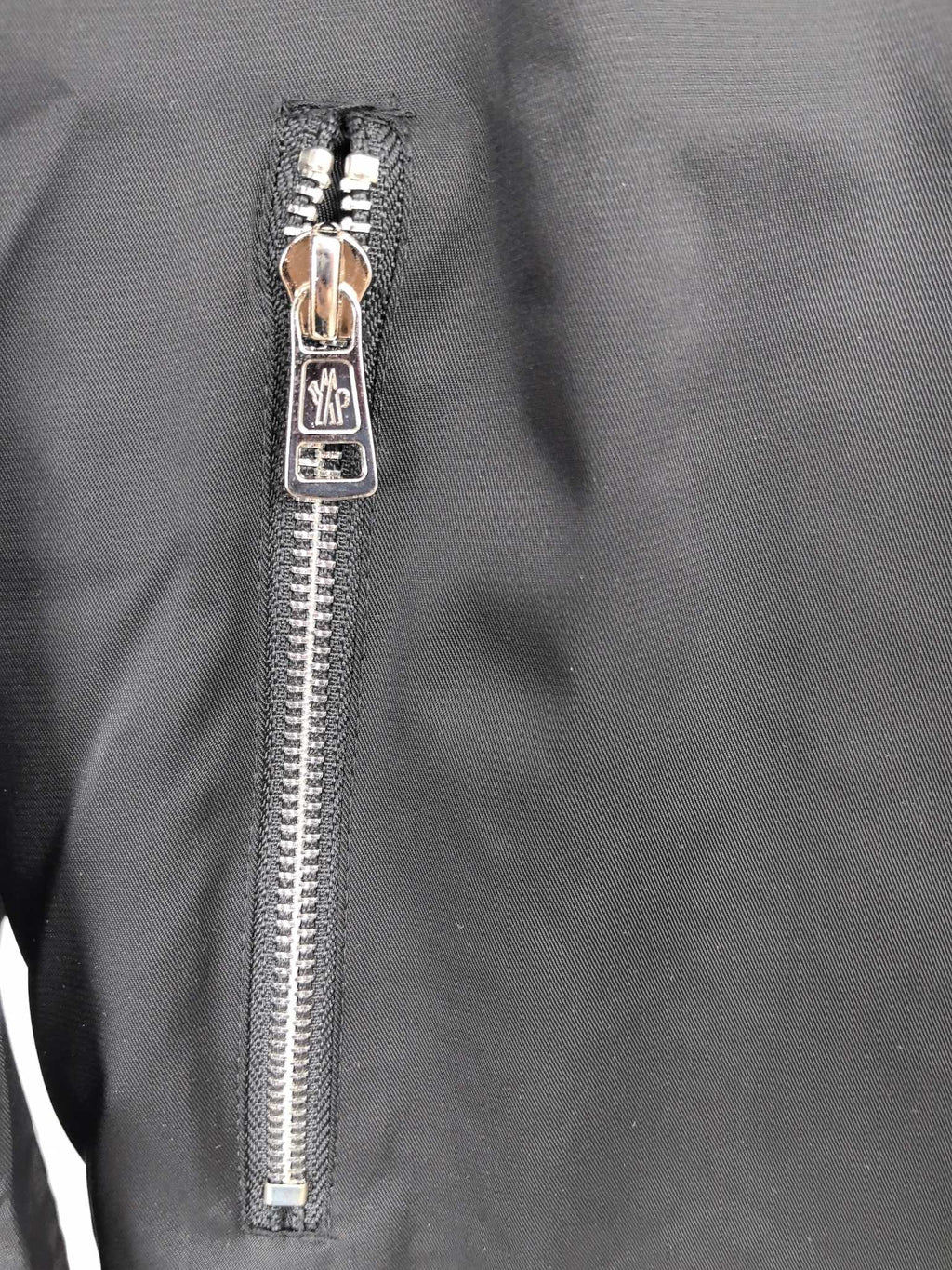Black jacket front zipper close-up with metal pull and teeth.