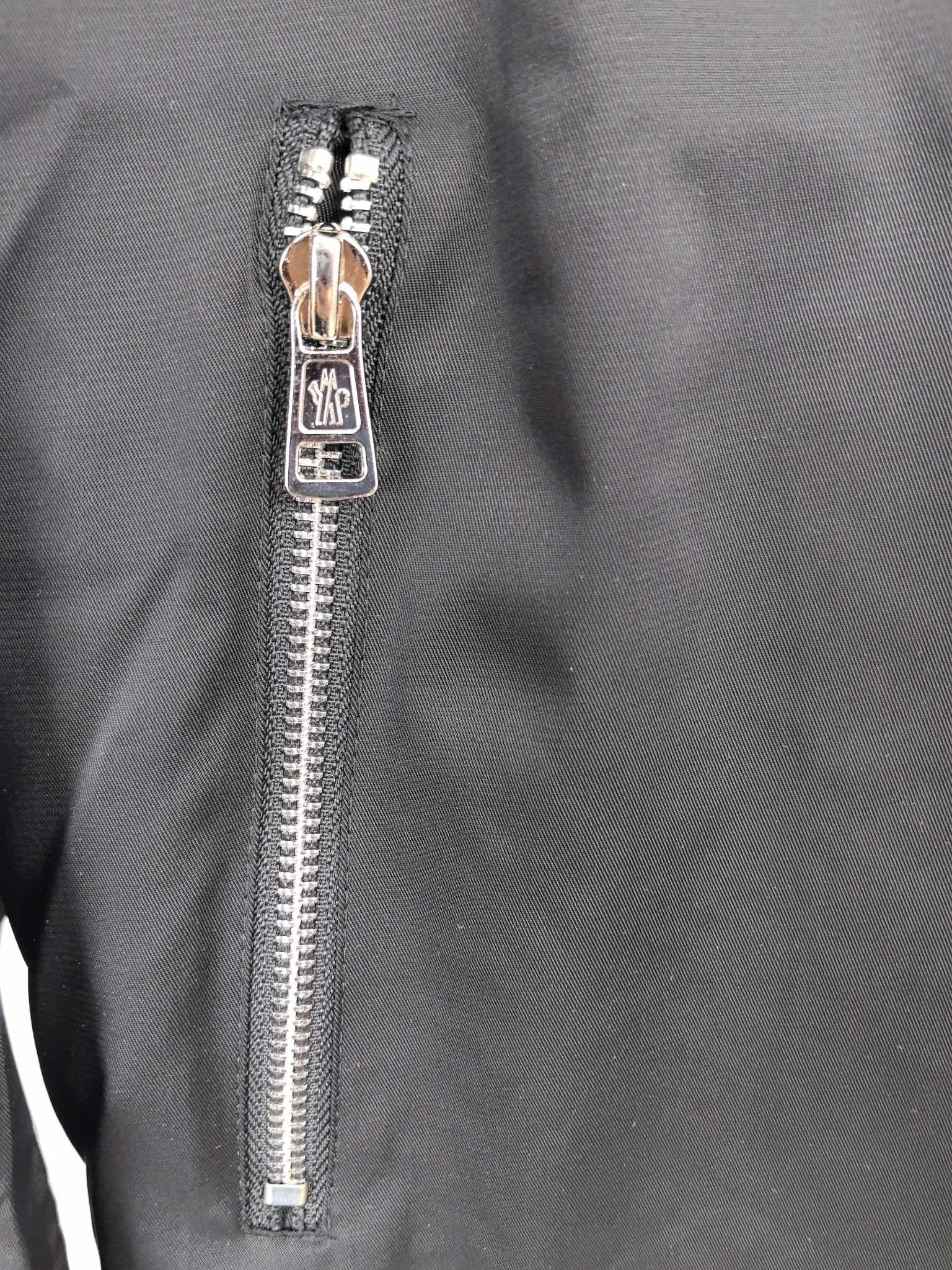 Black jacket front zipper close-up with metal pull and teeth.
