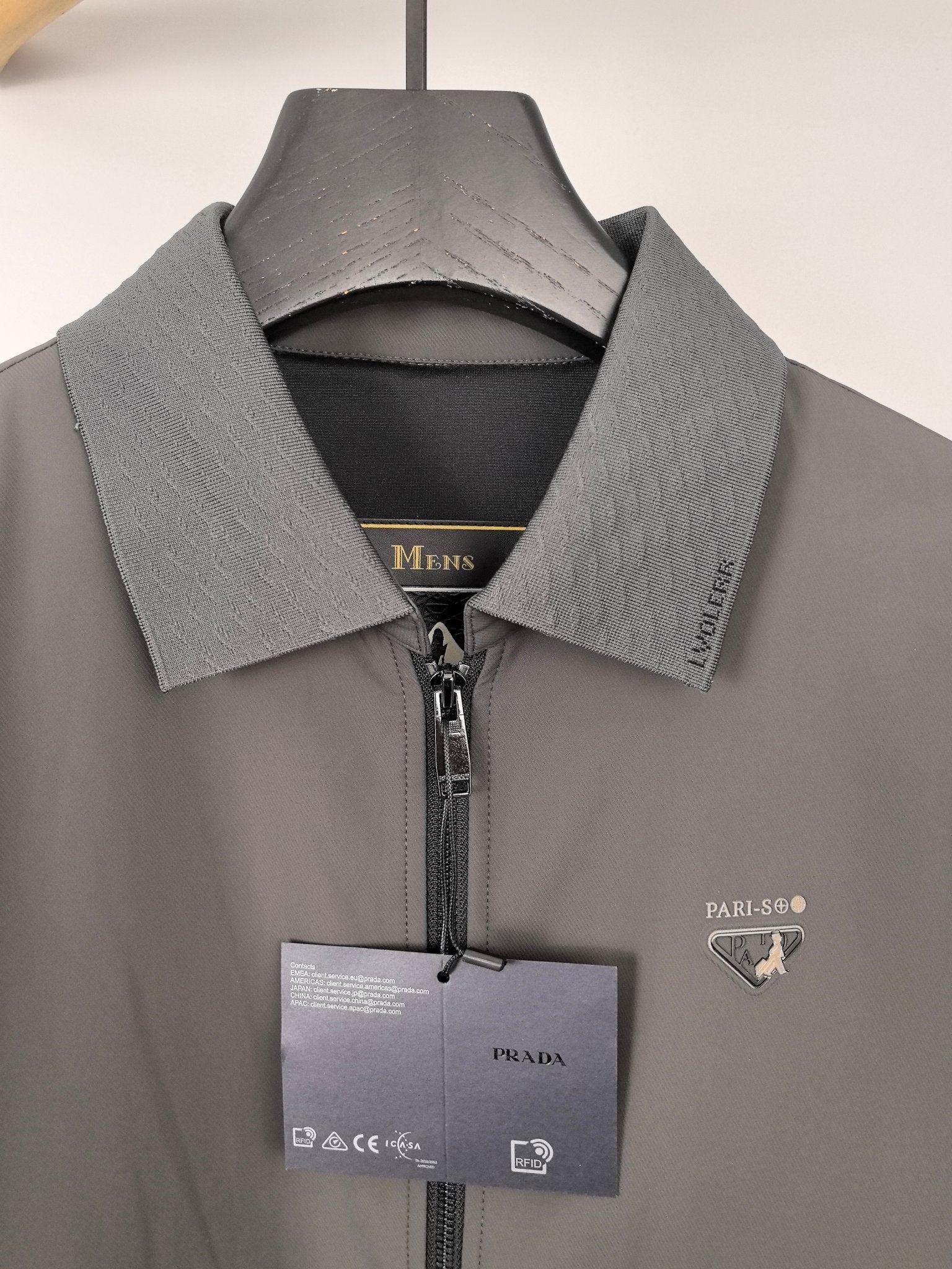 Prada jacket close-up at collar and zipper, dark gray with hanging logo tag