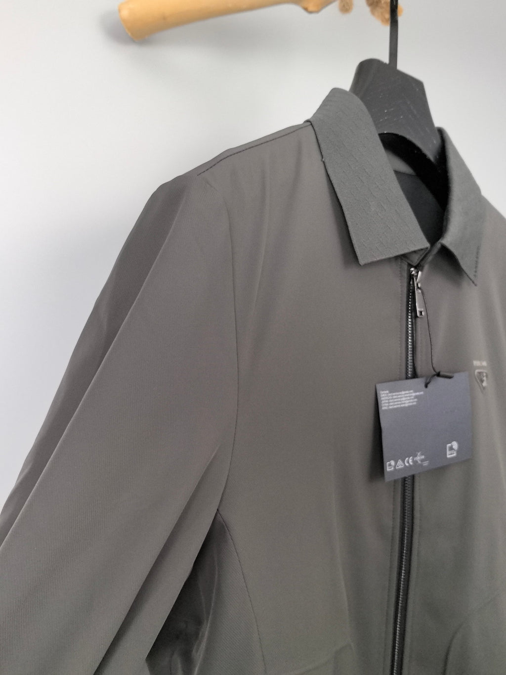 Prada zip-up jacket side view with dark gray fabric, front zipper, and tag