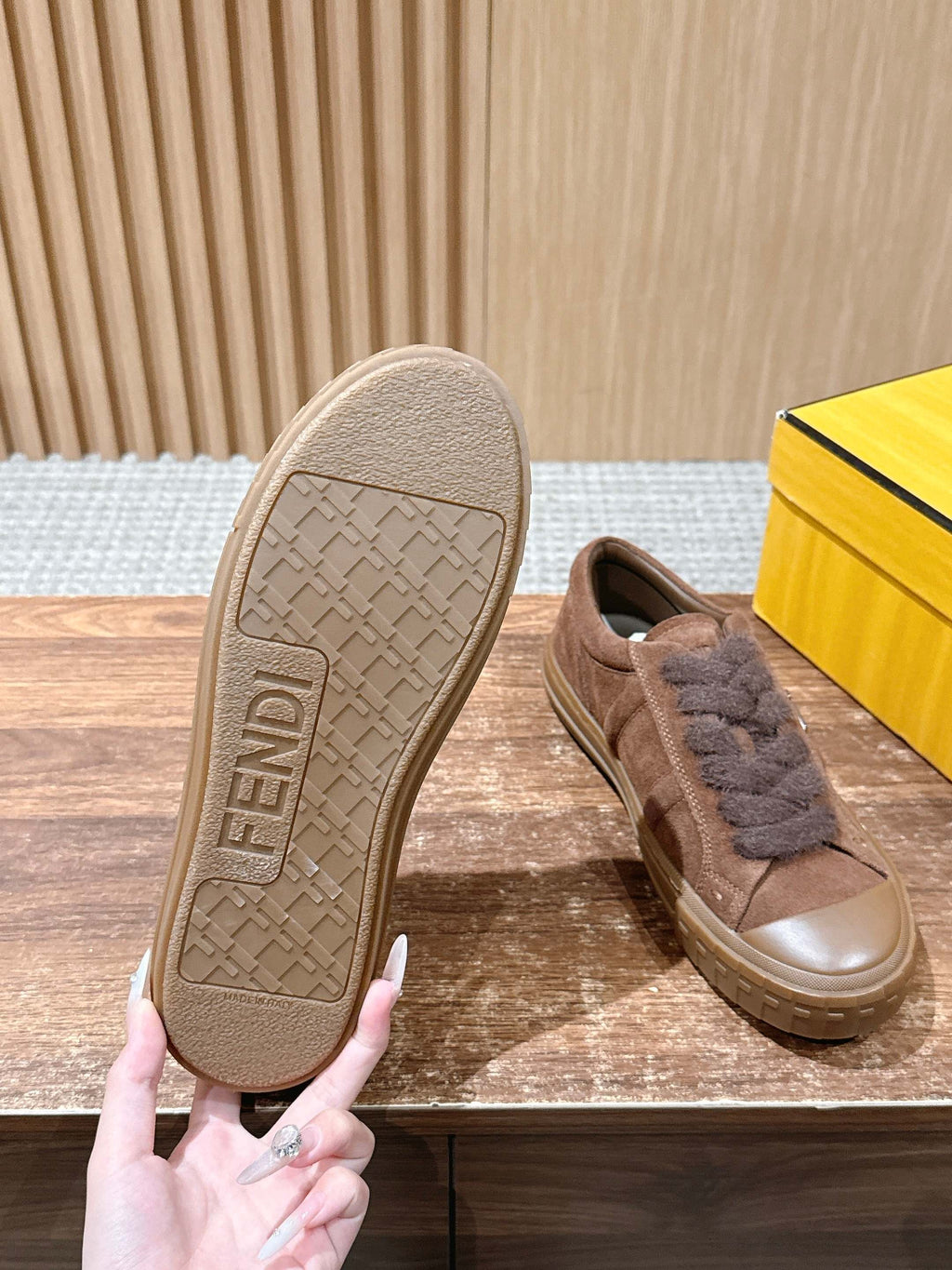 Fendi-branded outsole on brown suede sneaker with fuzzy laces, paired with another