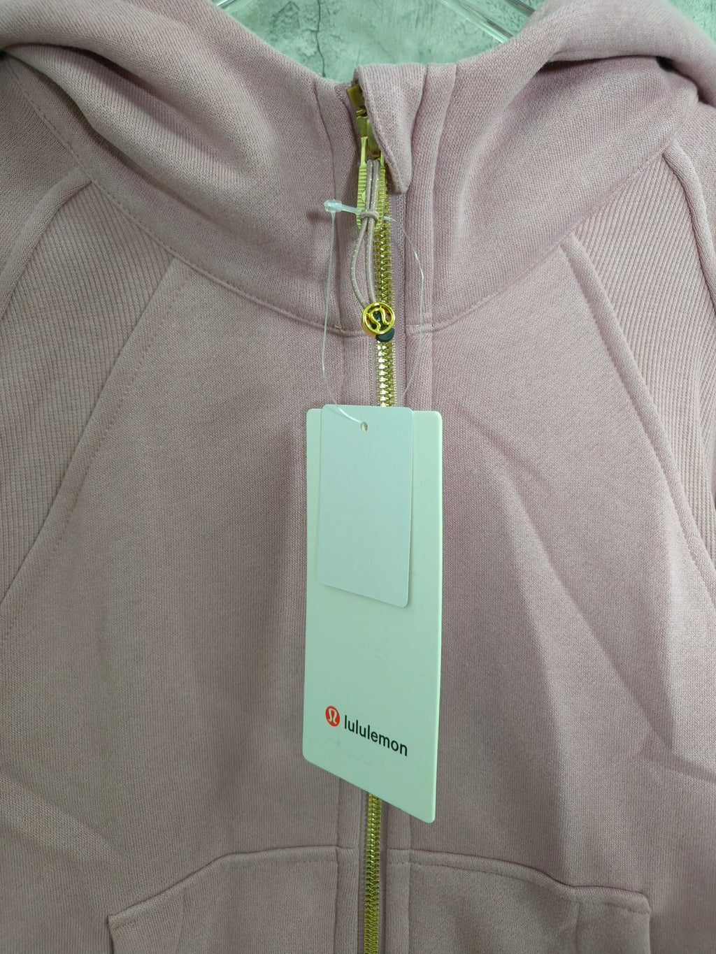 Light pink zip-up hoodie close-up with hood, zipper, and hanging tag