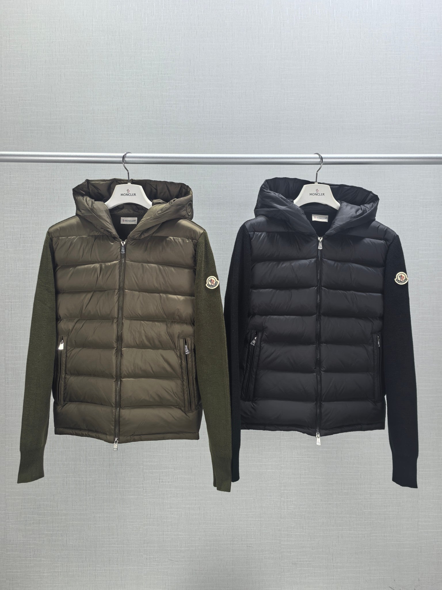 Two Moncler hooded puffer jackets on hangers: olive and dark, full zip