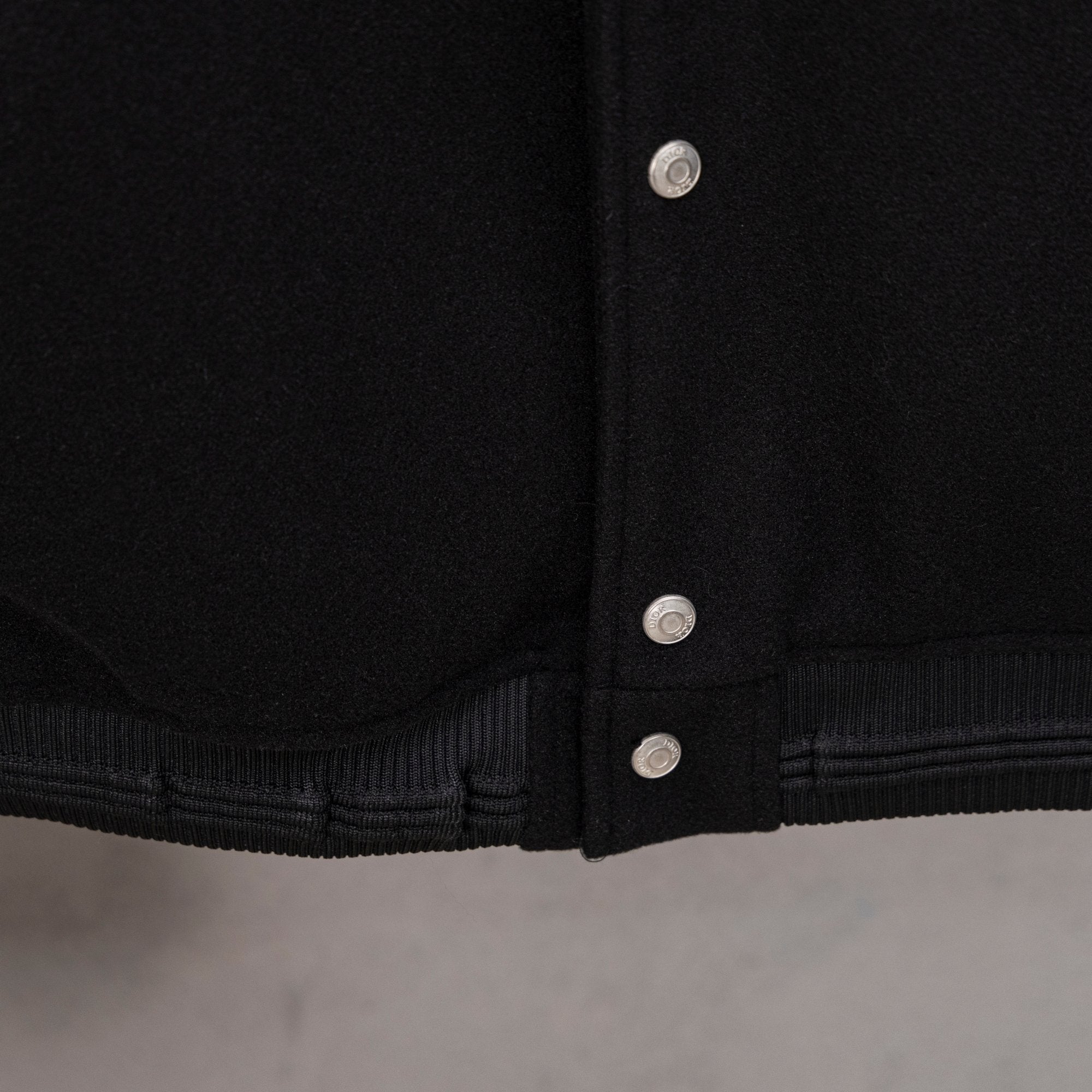 Black varsity jacket hem with ribbed cuffs and three button placket