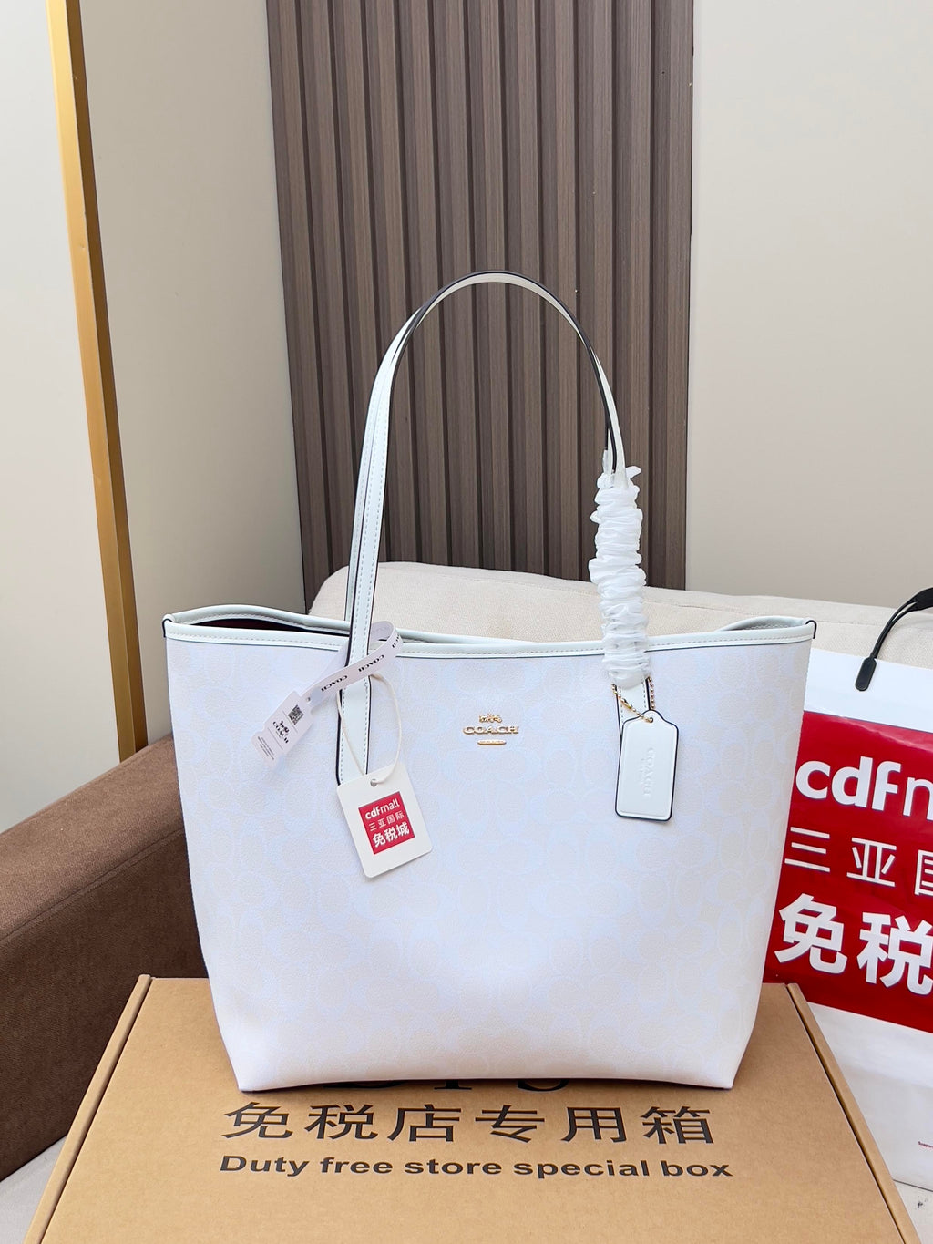 Coah white tote bag with long handles, tags attached, sitting on box