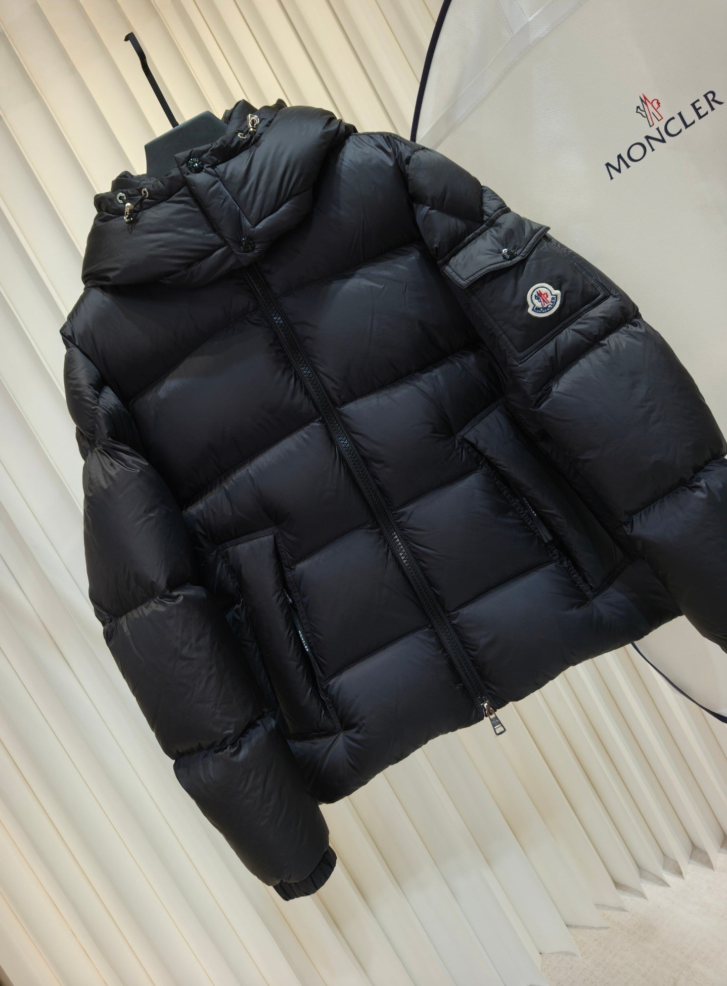 Moncler long padded jacket in dark color, quilted puffer with hood and side sleeve patch