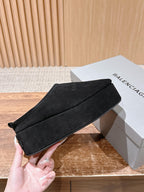 Black suede slip-on mule being held, with stitched upper and rounded toe