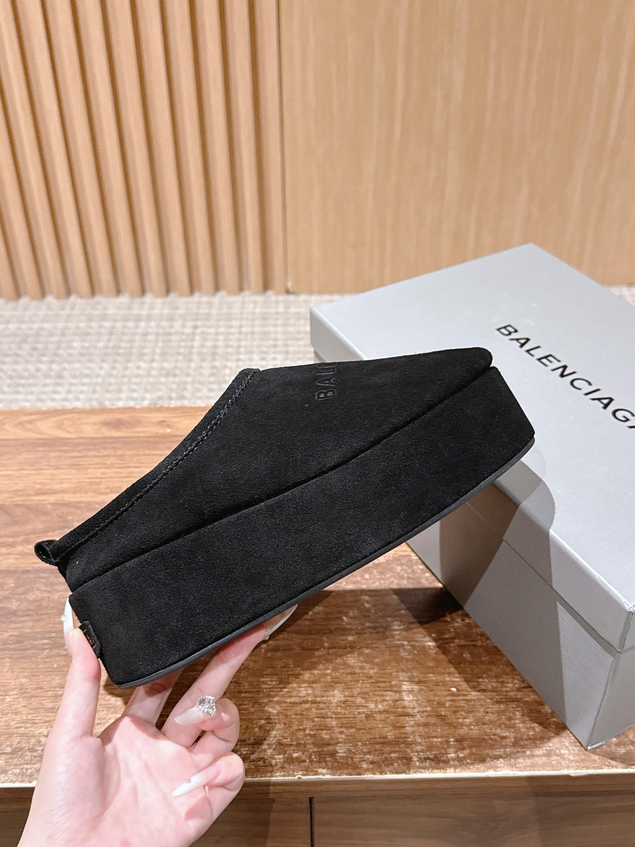 Black suede slip-on mule being held, with stitched upper and rounded toe