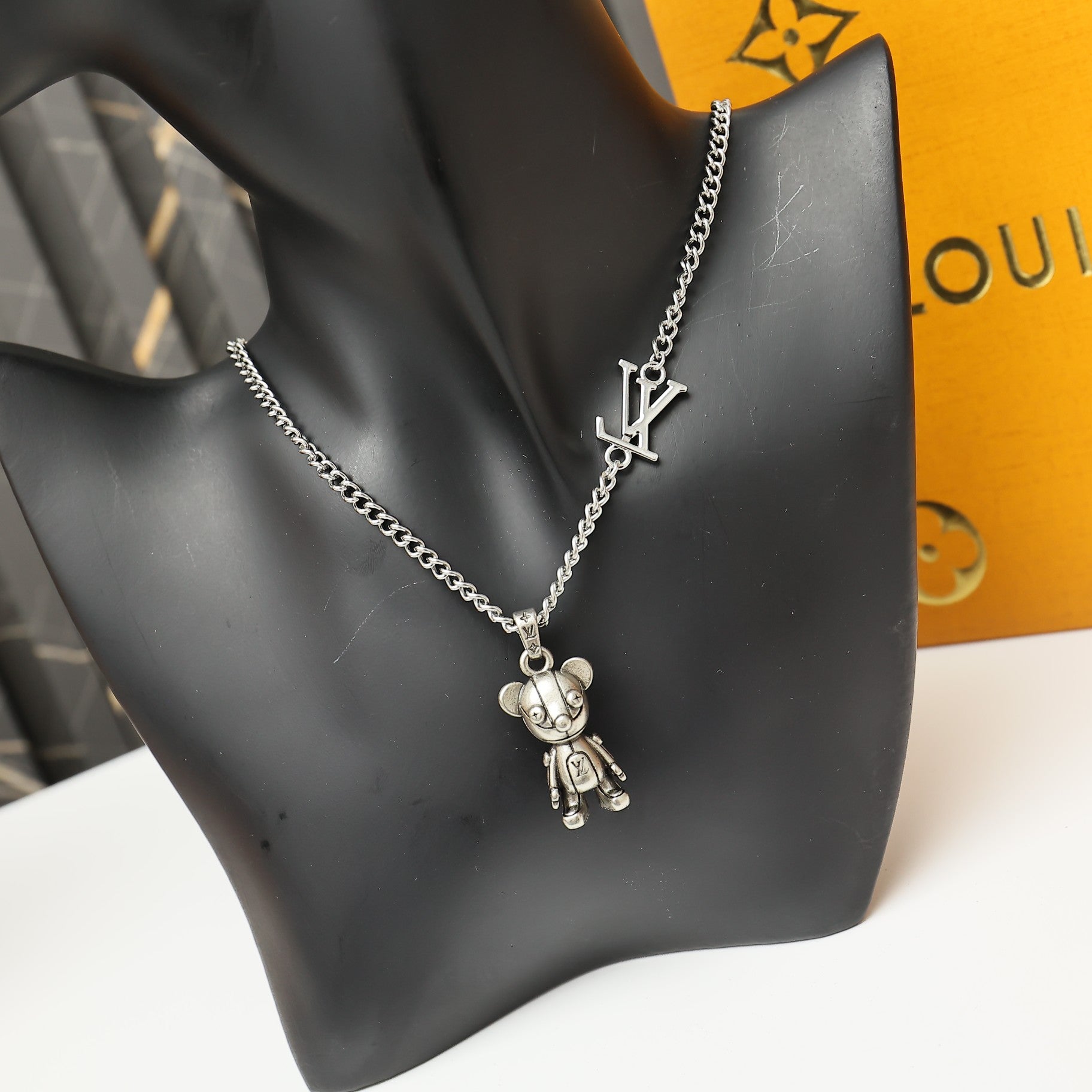 Silver chain necklace on a black bust with LV logo charm and bear pendant