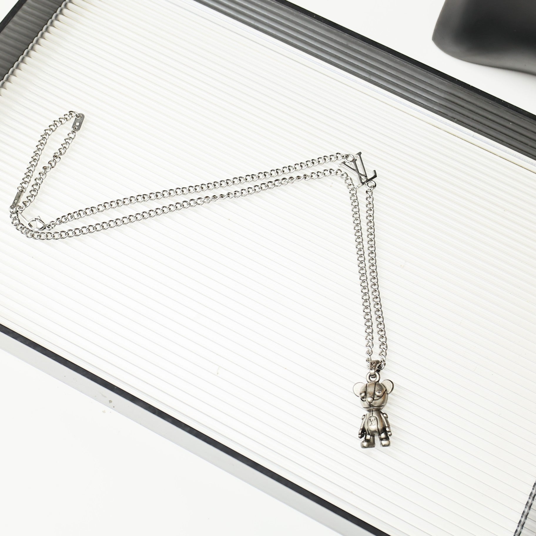 Silver chain necklace with a hanging bear charm on a white ridged book