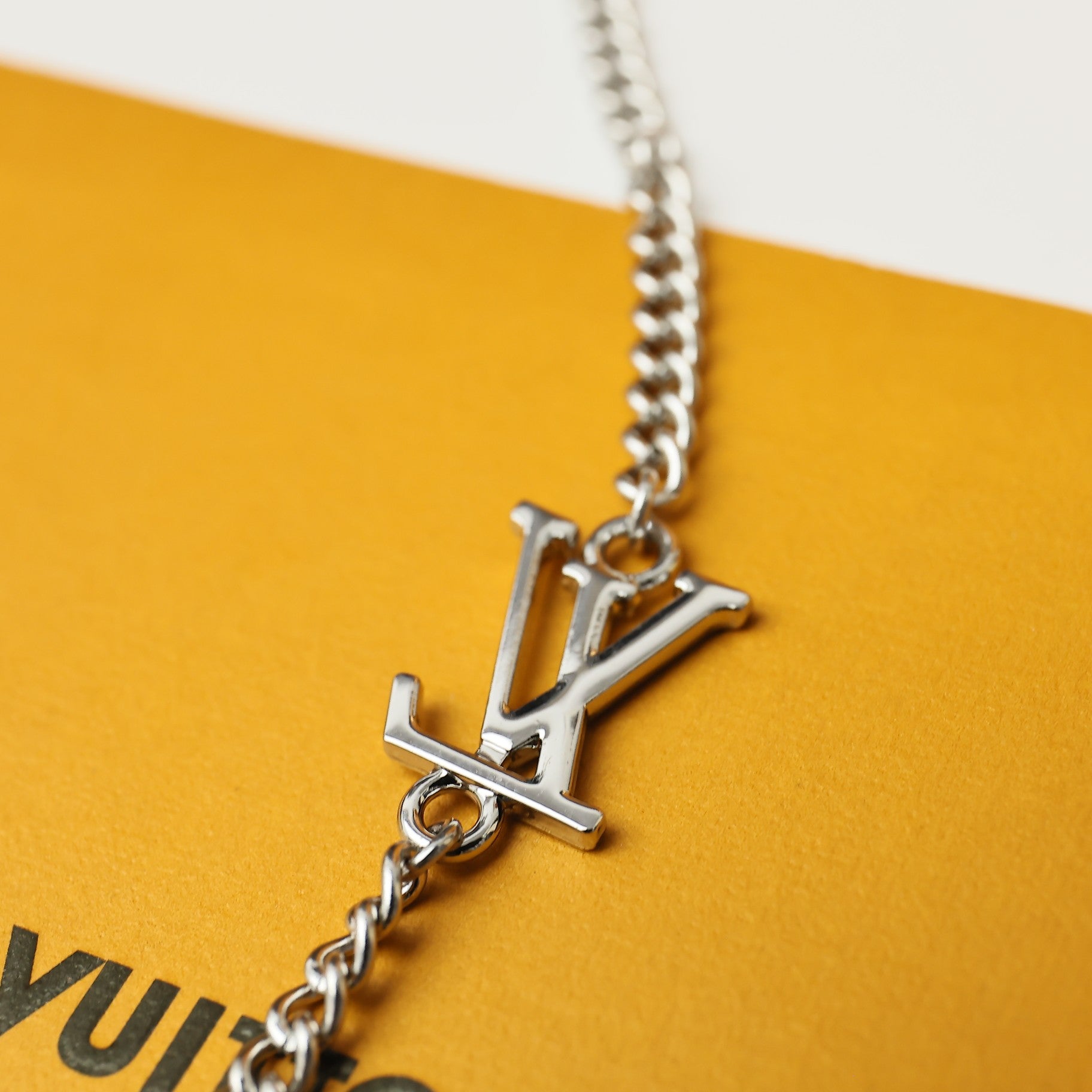 Silver LV logo pendant with chain on a yellow card