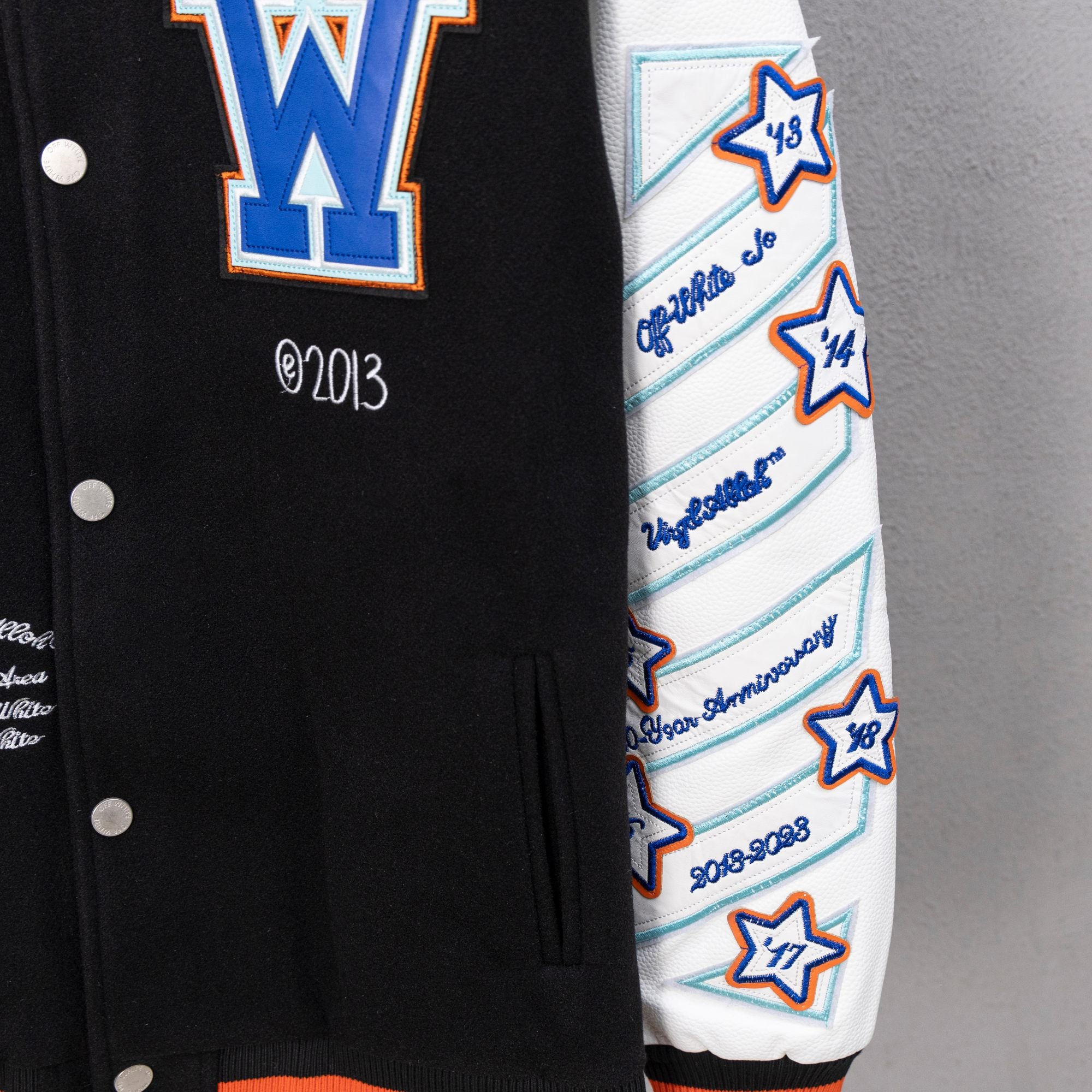 Varsity jacket sleeve with white base, blue stripes, star patches, and knit cuff.