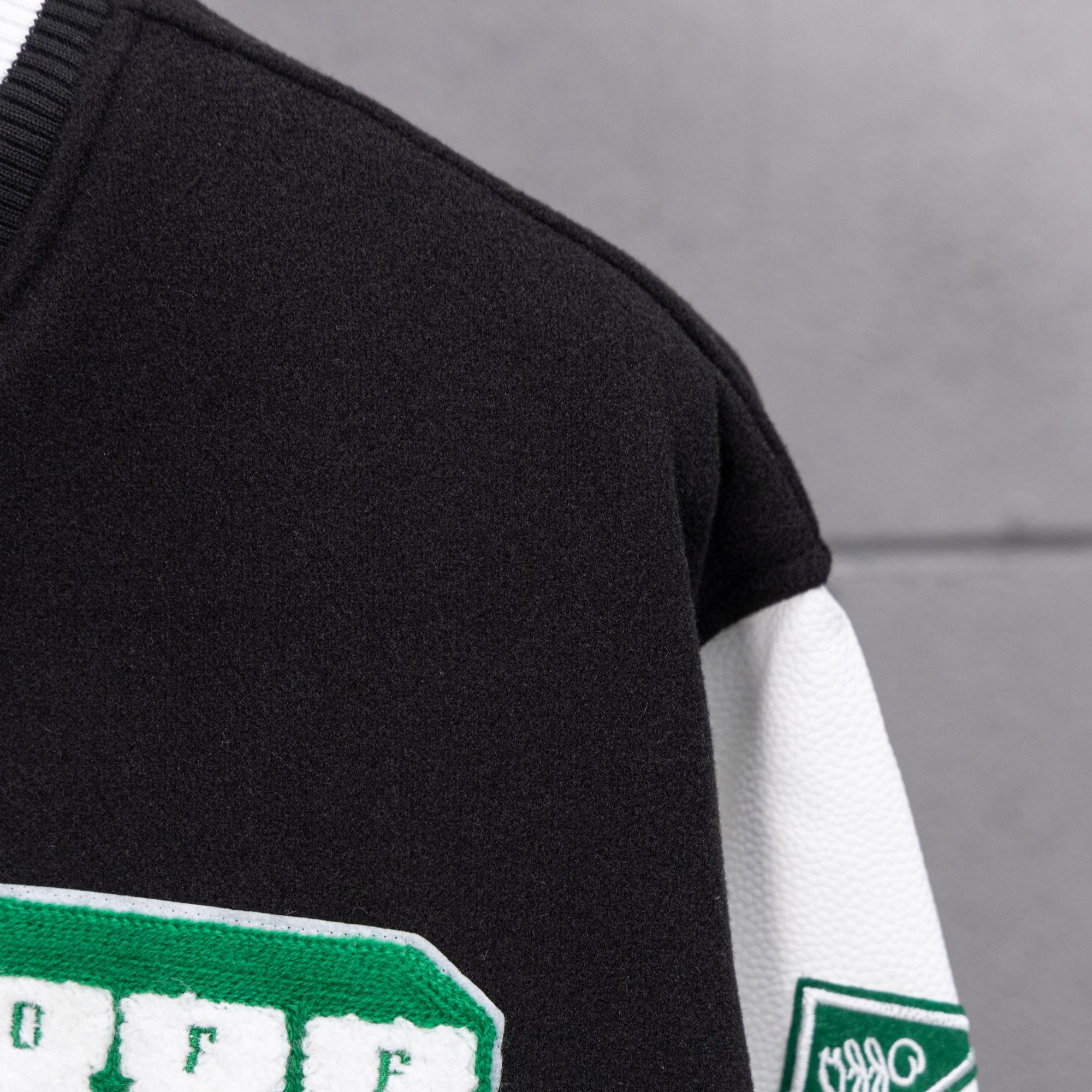 Black varsity jacket sleeve with green patch detail and white striped cuff