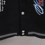 Black varsity jacket front with snap buttons and striped ribbed hem trim.