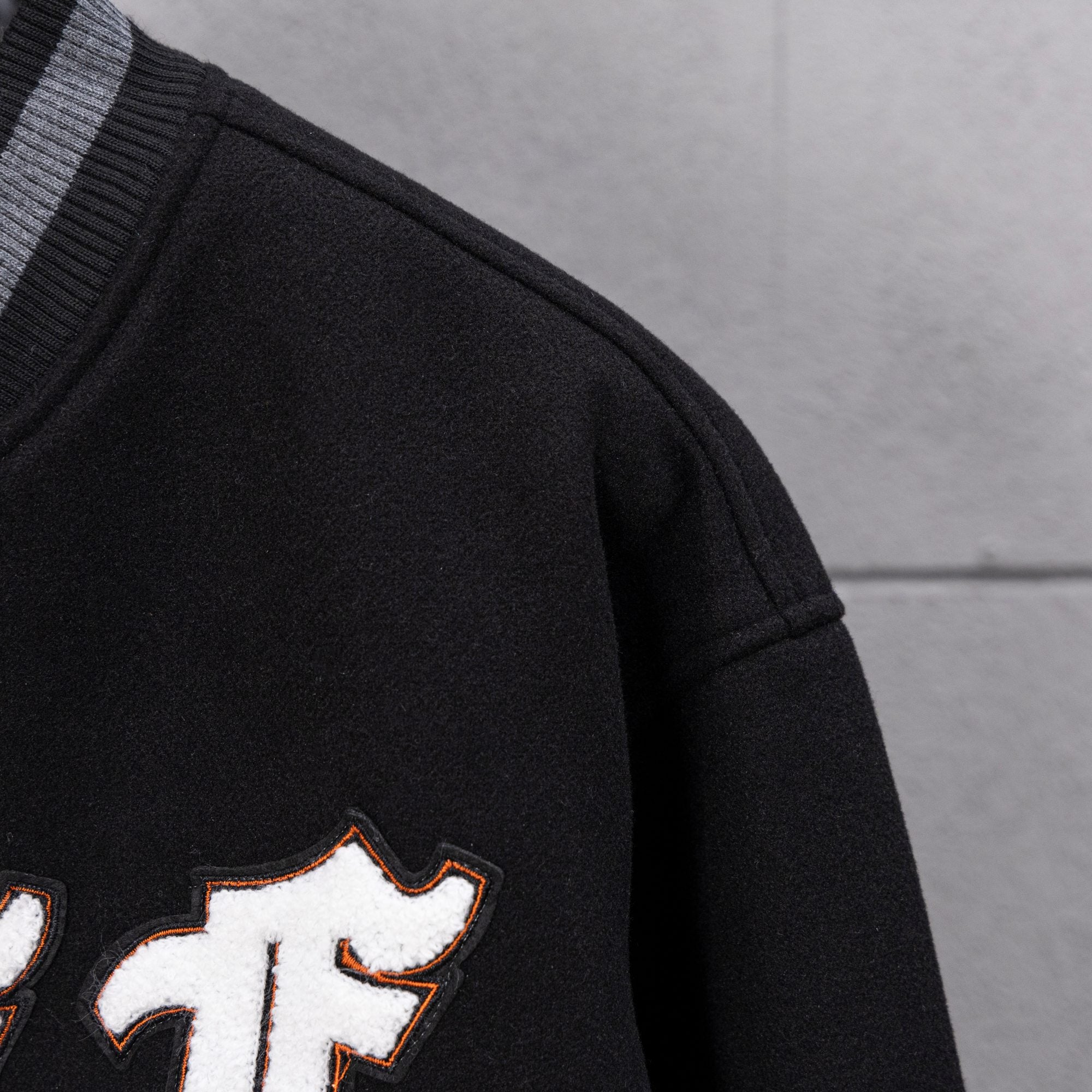 Black varsity jacket sleeve with striped rib cuff and partial embroidered lettering.