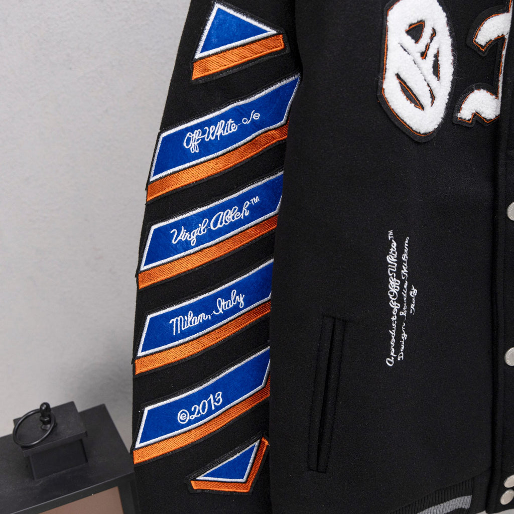 Black varsity jacket sleeve with orange-blue striped graphic patch and cursive text.