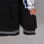 Black varsity jacket sleeve cuff with striped ribbing and character graphic patch.