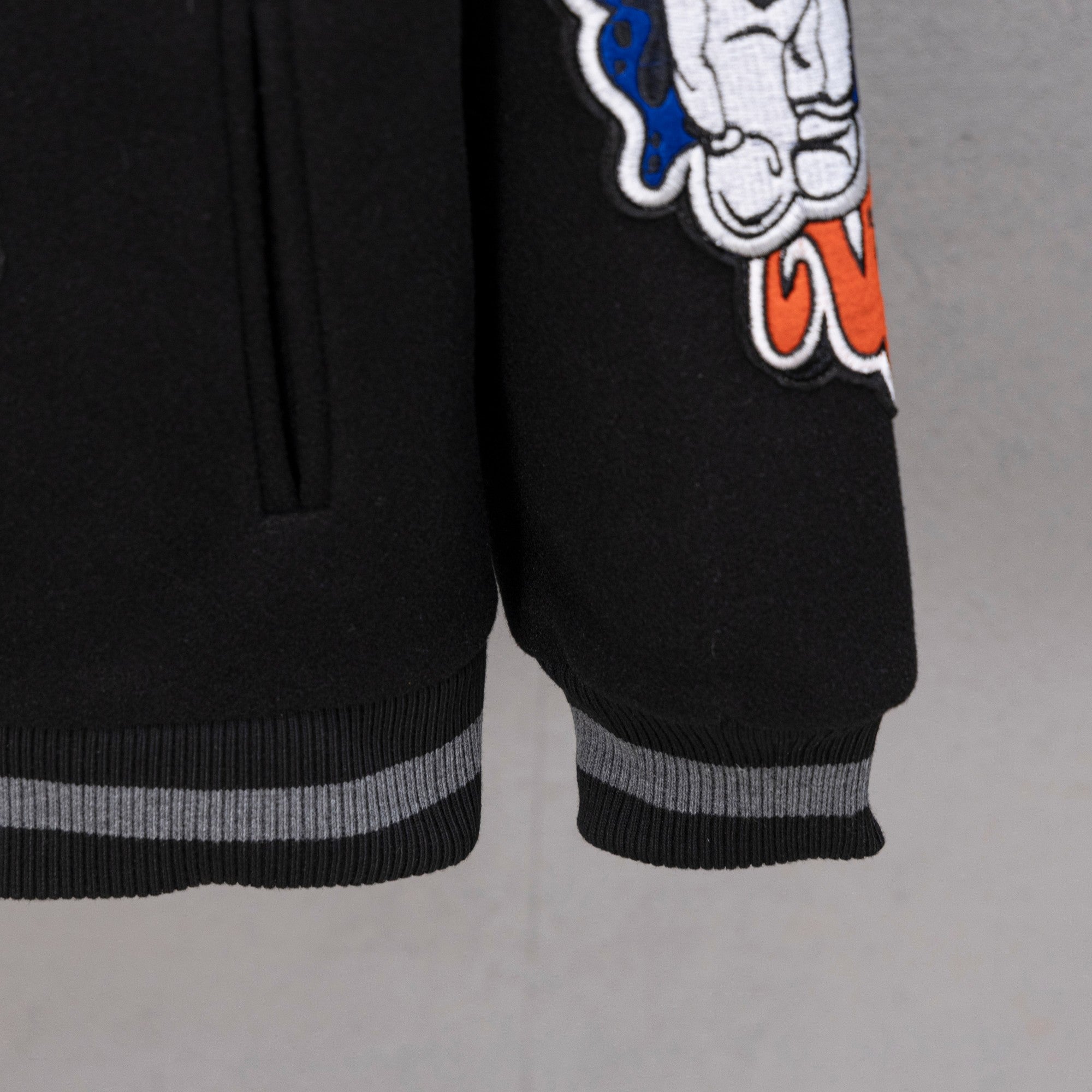 Black varsity jacket sleeve cuff with striped ribbing and character graphic patch.