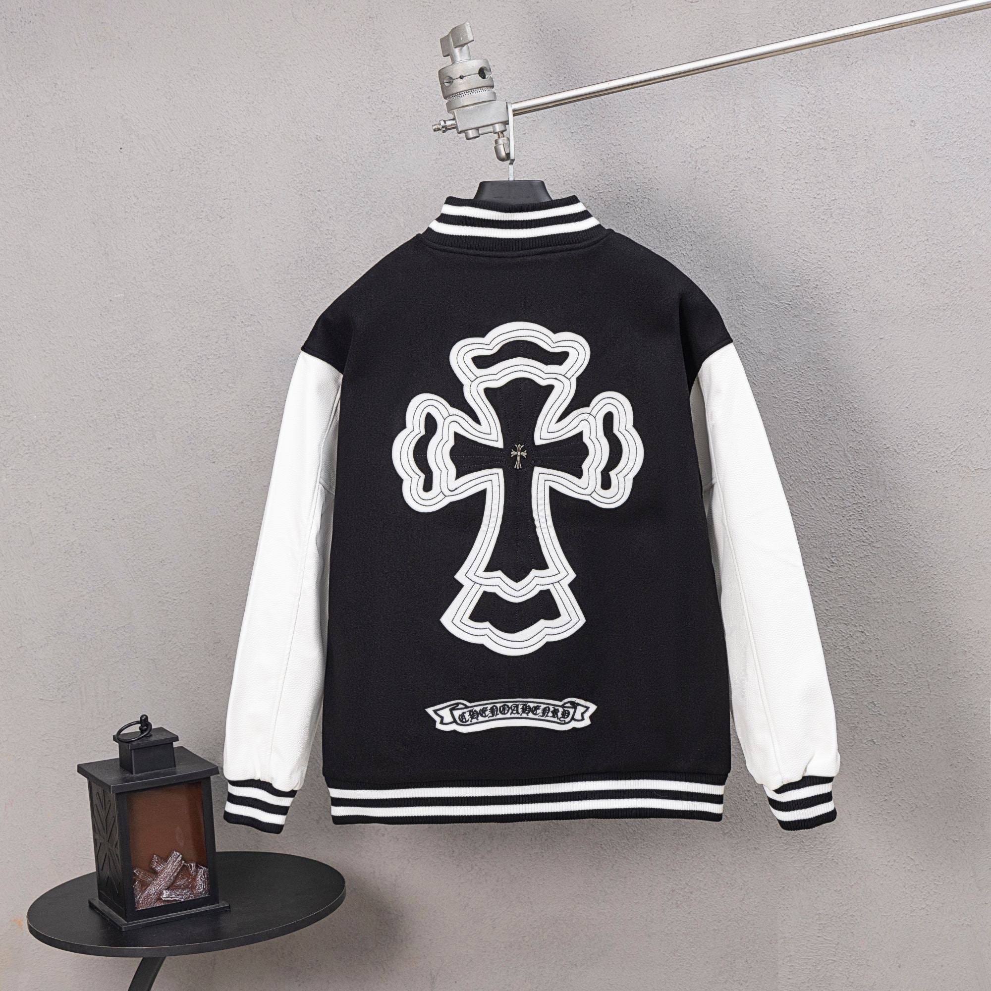 Black varsity jacket with large white cross graphic and striped ribbed cuffs