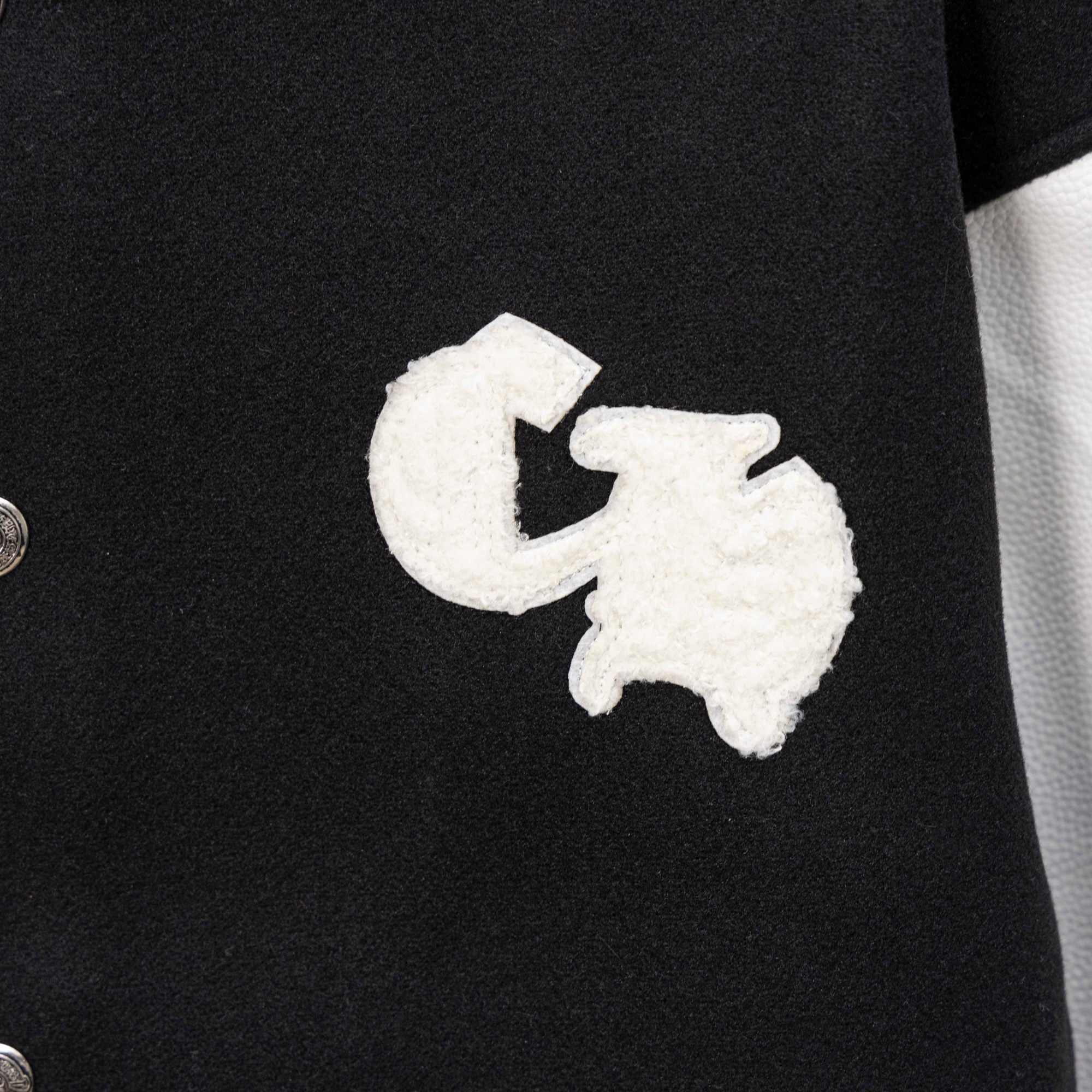 White embroidered cross motif on black varsity jacket front