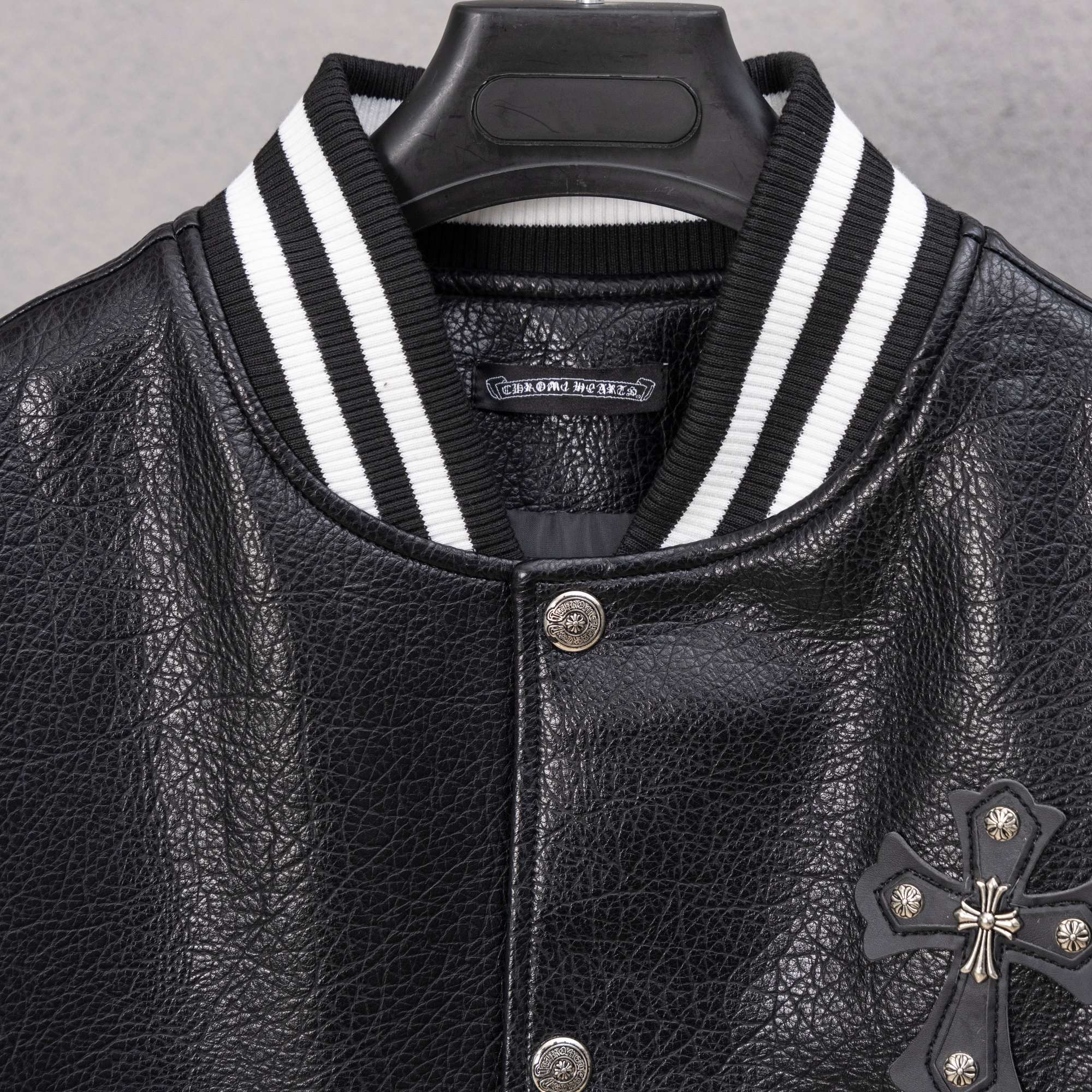 Black leather varsity jacket close-up with white striped collar and snap buttons
