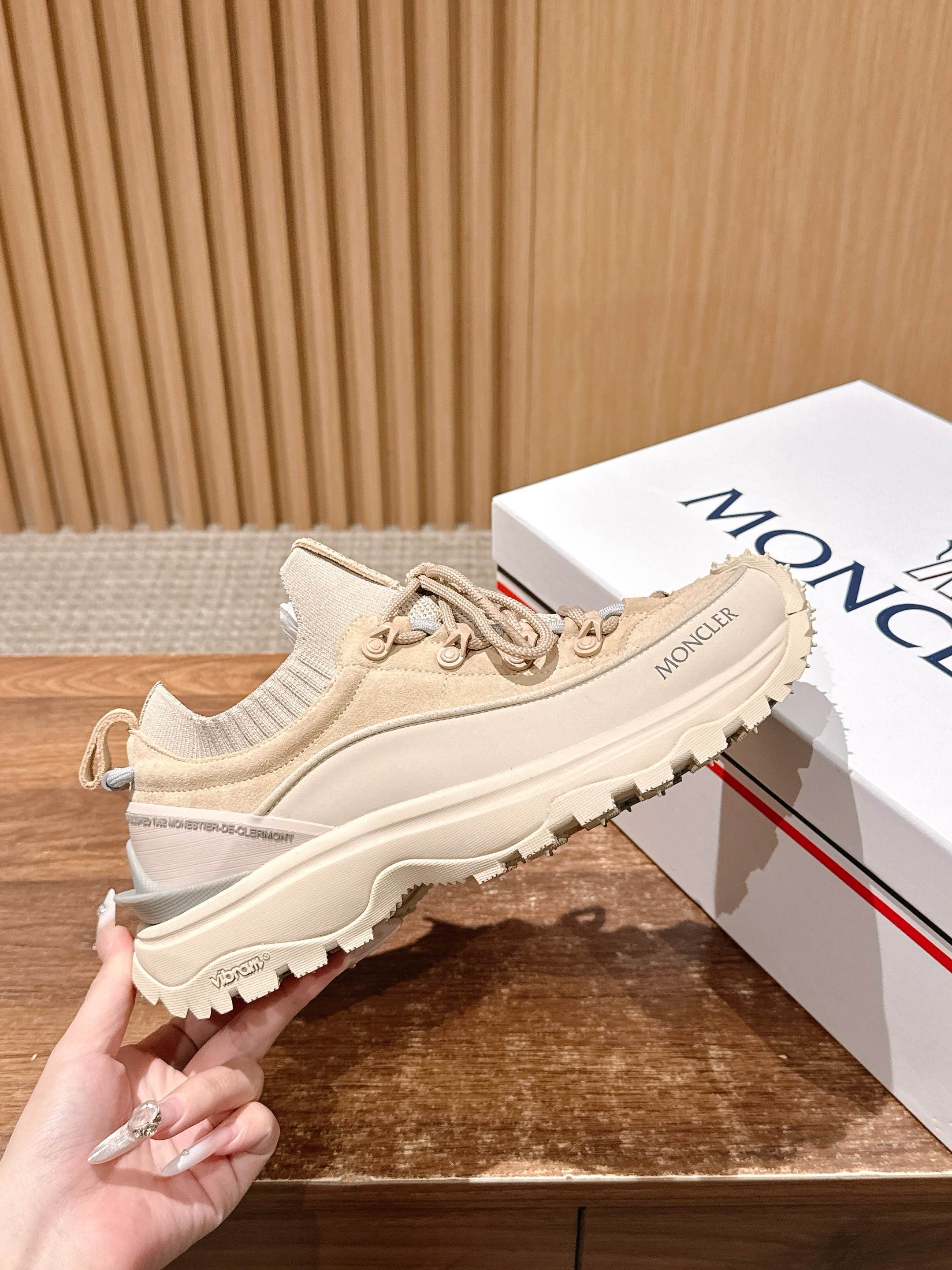 Moncler beige lace-up sneaker held in hand, side profile with rugged sole.