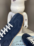 Prada dark blue suede sneaker side view with white laces and gum sole.