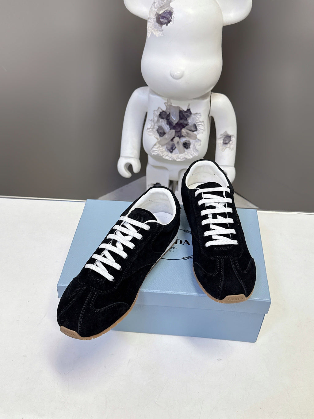 Black suede unisex sneakers with white laces, side view on box.