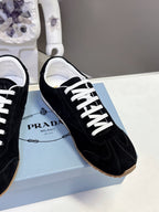 Black suede sneaker detail with white laces and Prada logo on tongue.