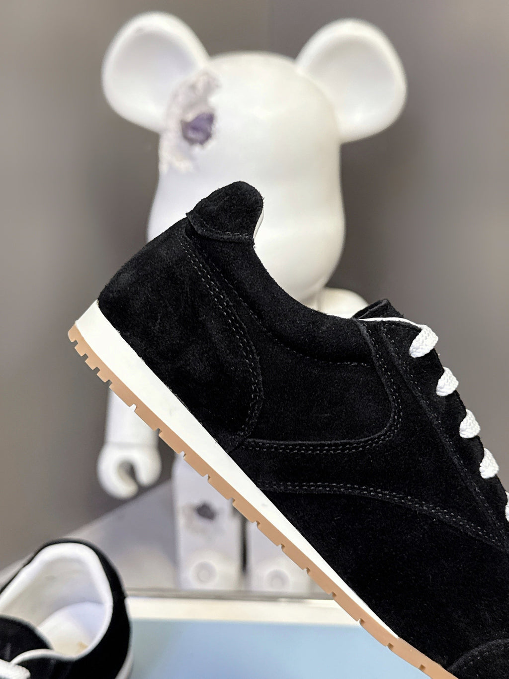 Black suede low-top unisex sneaker with white laces and tan rubber sole.
