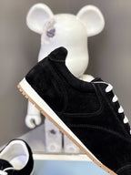 Black suede low-top unisex sneaker with white laces and tan rubber sole.