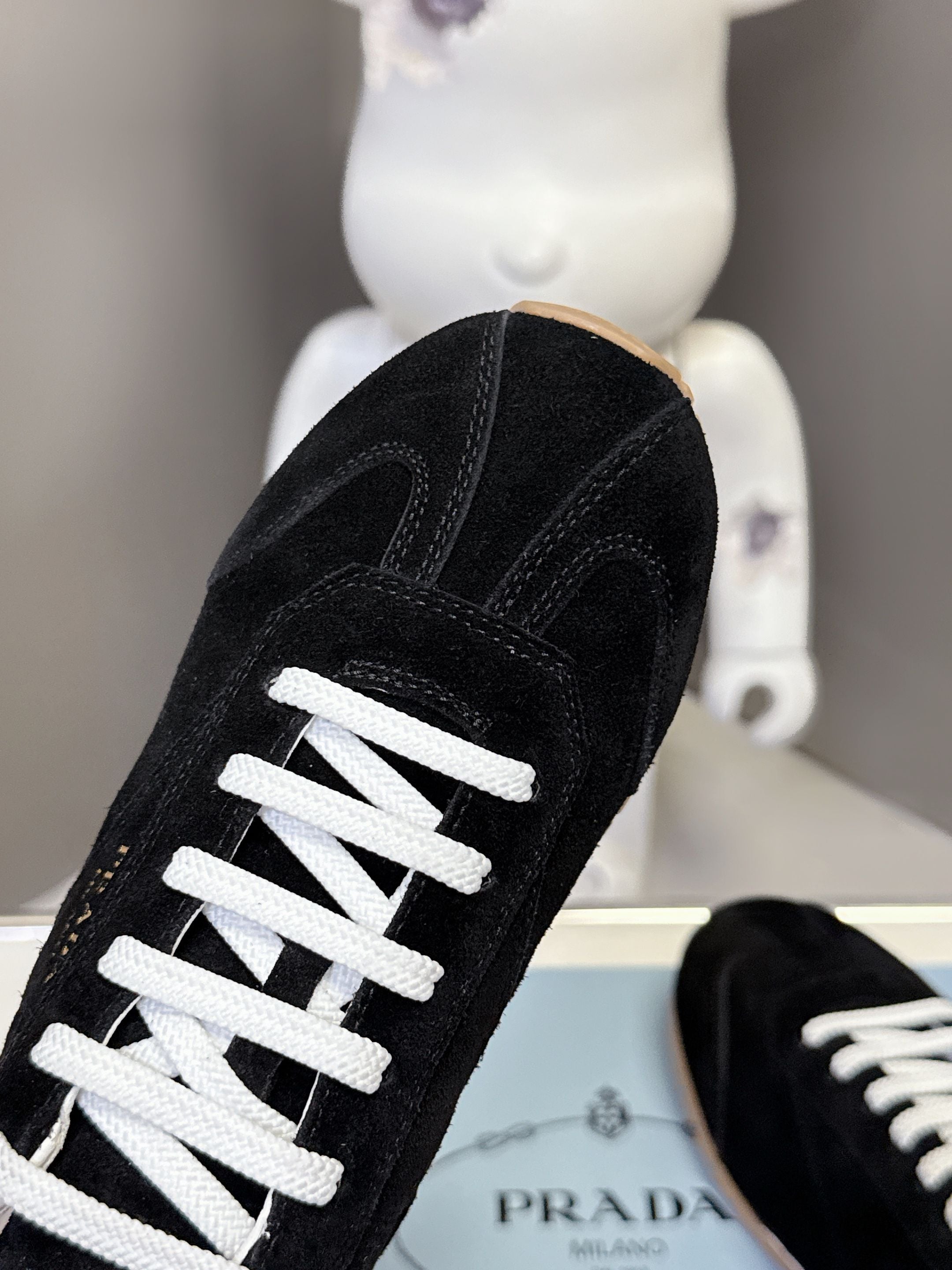 Black suede sneaker side with white lace-up and padded collar detail.