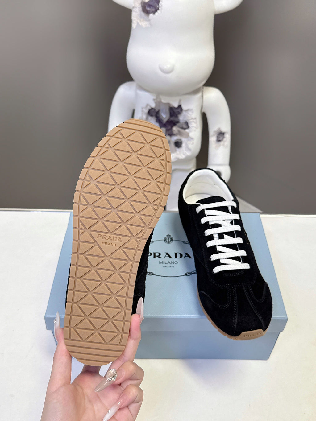 Back sole view of black unisex sneakers with tan textured outsole on box.
