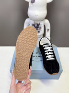 Back sole view of black unisex sneakers with tan textured outsole on box.
