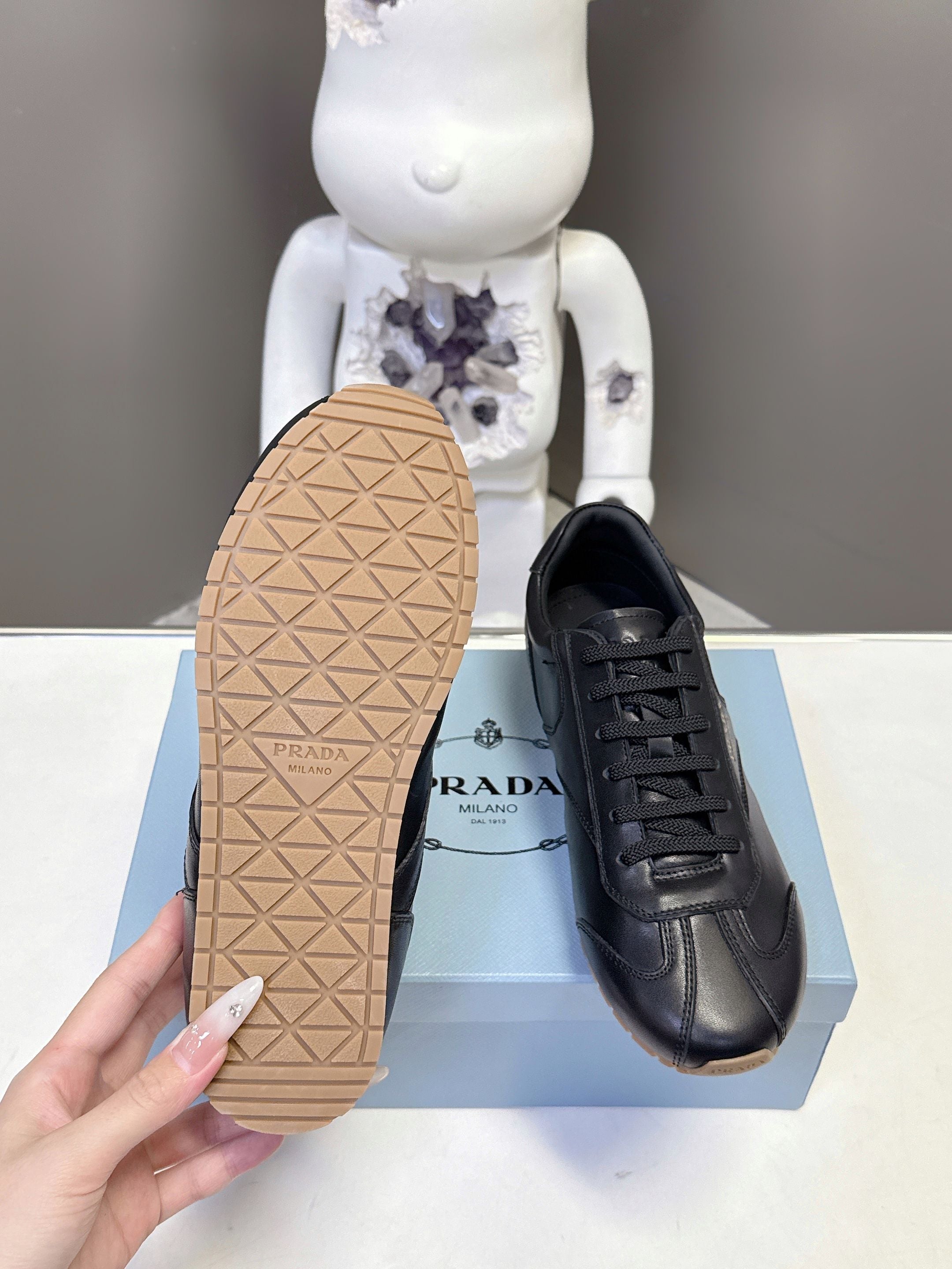 Black leather lace-up sneaker showing tan textured outsole and stitched upper