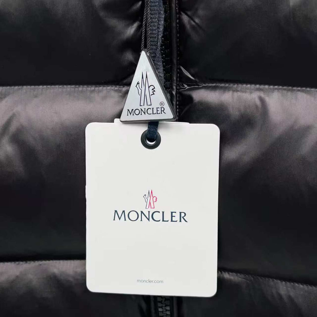 Moncler puffer jacket garment tag on dark quilted fabric with zipper pull area