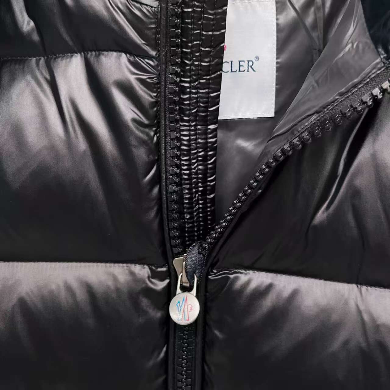 Moncler puffer jacket close-up, dark color, full-zip front with metal zipper pull