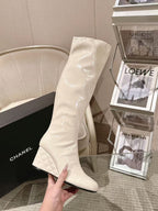 Chanel light white knee-high boot held in hand, quilted sole edge and pointed toe