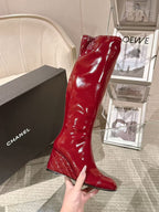 Red patent leather knee boot held in hand, glossy finish