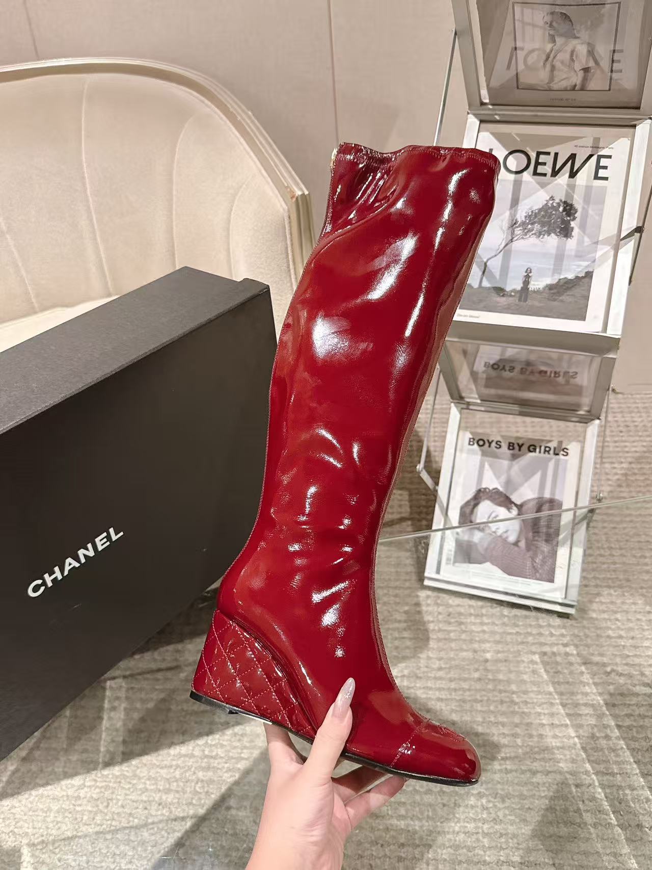 Red patent leather knee boot held in hand, glossy finish