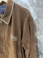 Brown jacket sleeve with white-trimmed edge and cursive logo embroidery