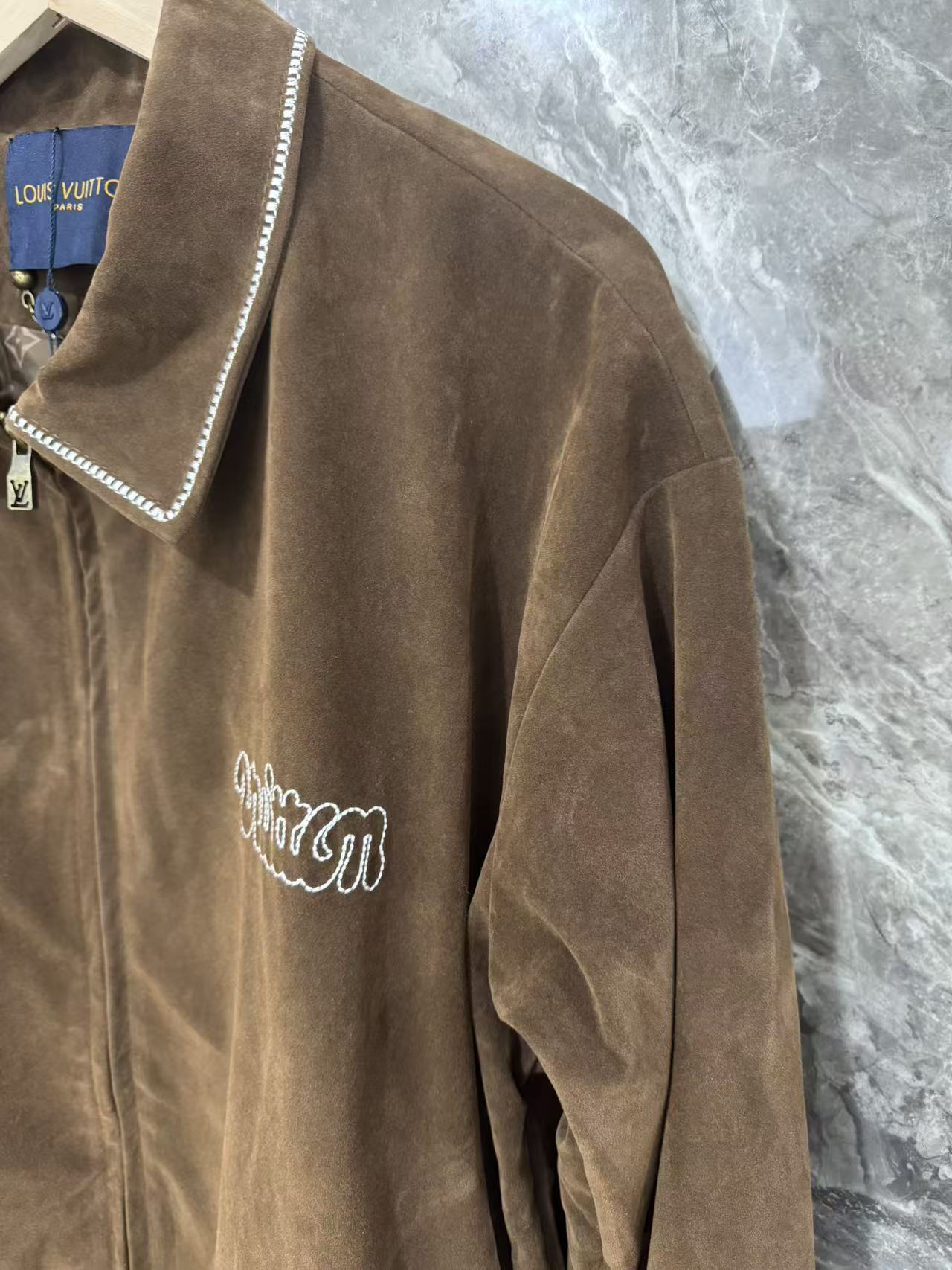 Brown jacket sleeve with white-trimmed edge and cursive logo embroidery